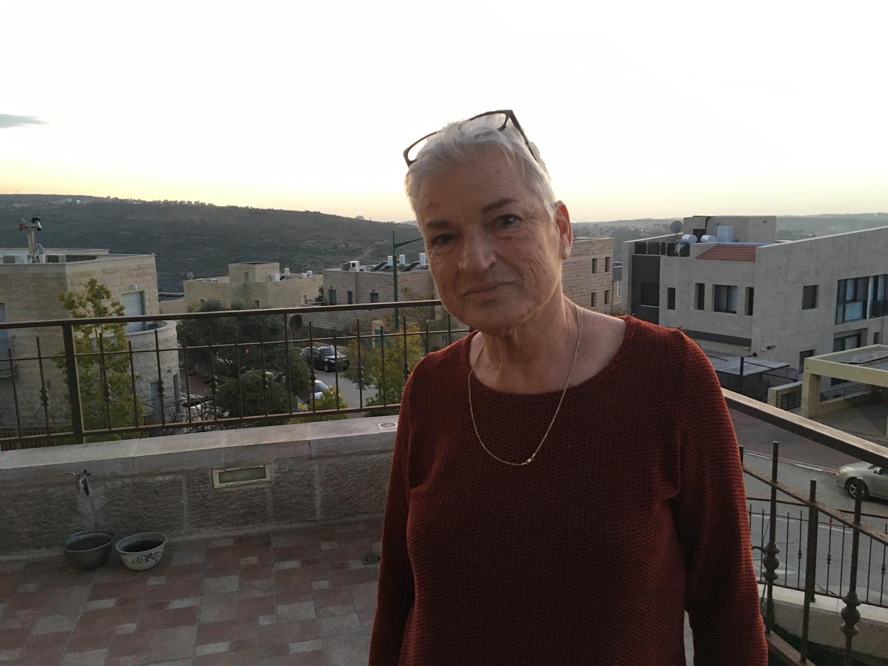 Eine ältere Frau mit kurzen Haaren steht auf einer Terrasse.
