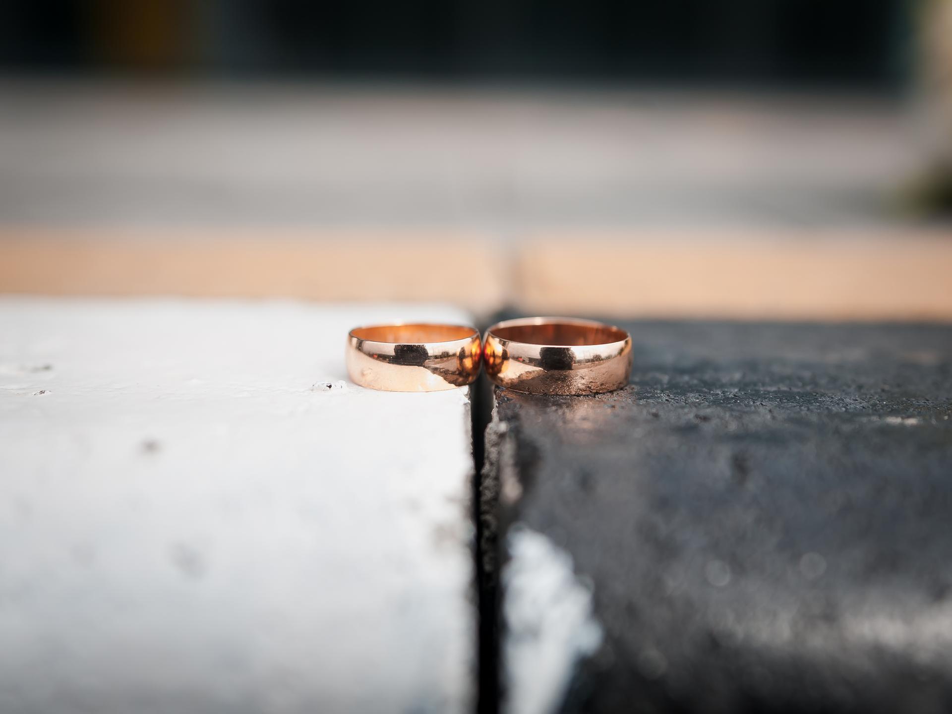 Zwei goldene Eheringe liegen nebeneinander. Der linke Ring liegt auf einem weißen, der rechte Ring auf einem schwarzen Untergrund.
