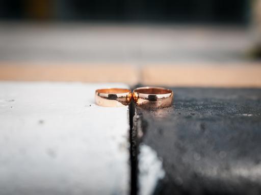 Zwei goldene Eheringe liegen nebeneinander. Der linke Ring liegt auf einem weißen, der rechte Ring auf einem schwarzen Untergrund.