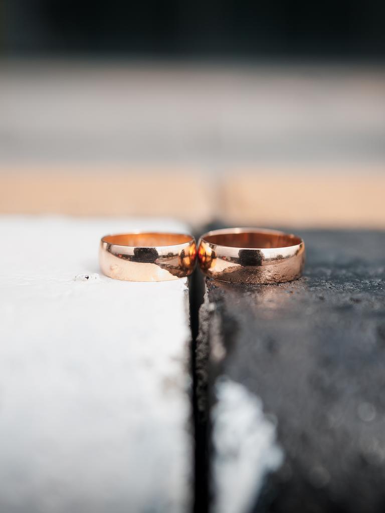 Zwei goldene Eheringe liegen nebeneinander. Der linke Ring liegt auf einem weißen, der rechte Ring auf einem schwarzen Untergrund.