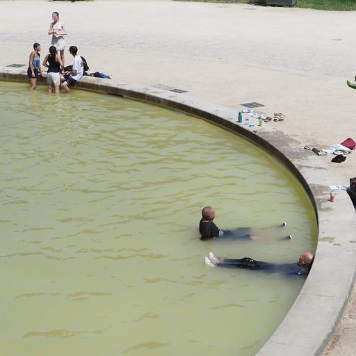 In einem Brunnen sitzen viele Menschen im Wasser. Einige tragen noch ihre Kleidung.