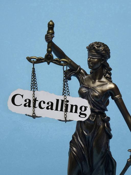 Eine Justizia-Stratue mit verbundenen Augen hat das Wort "Catcalling" auf den Waagschalen.