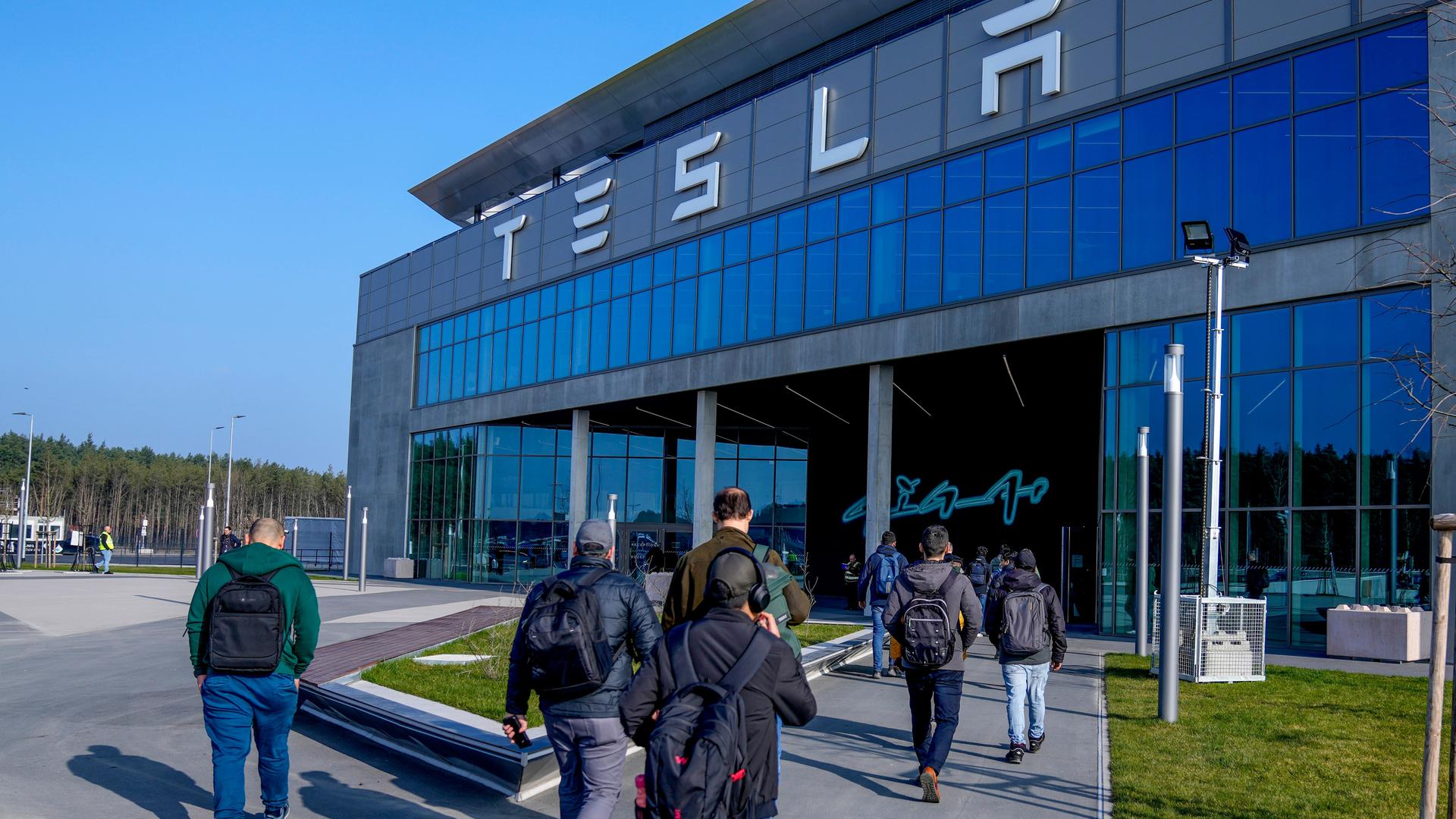 Arbeiter gehen unter blauem Himmel in das Tesla-Gebäude.