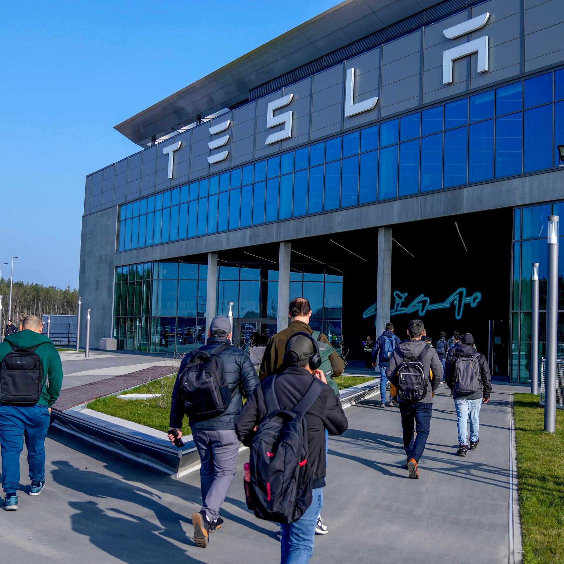Menschen laufen in das Gebäude der Tesla-Fabrik in Grünheide in Brandenburg, nachdem die Produktion nach einem Brandanschlag auf die Stromversorgung wieder angelaufen war. 
