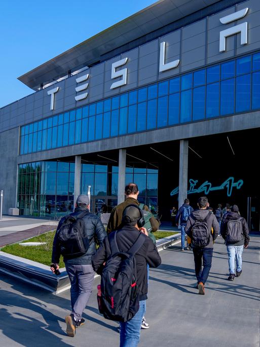 Menschen laufen in das Gebäude der Tesla-Fabrik in Grünheide in Brandenburg, nachdem die Produktion nach einem Brandanschlag auf die Stromversorgung wieder angelaufen war. 

