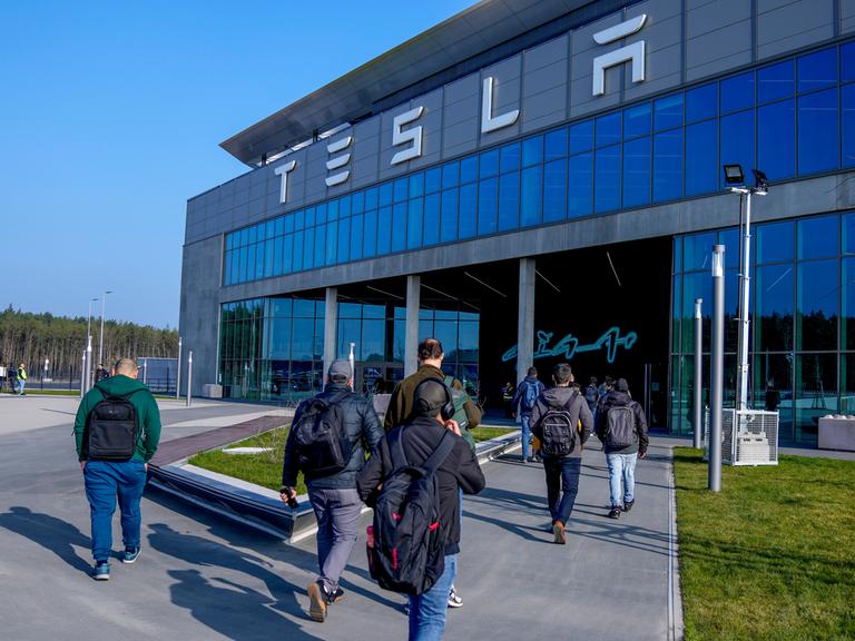 Menschen laufen in das Gebäude der Tesla-Fabrik in Grünheide in Brandenburg, nachdem die Produktion nach einem Brandanschlag auf die Stromversorgung wieder angelaufen war. 

