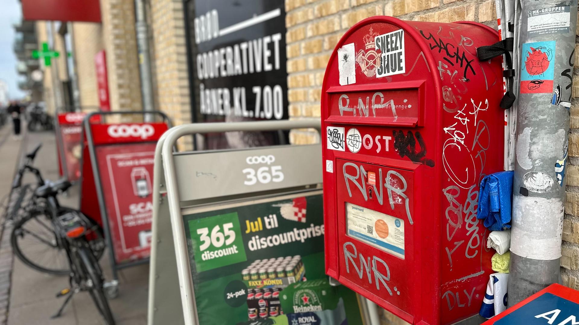 Ein roter Briefkasten der dänischen Post an der Außenwand eines Supermarkts
