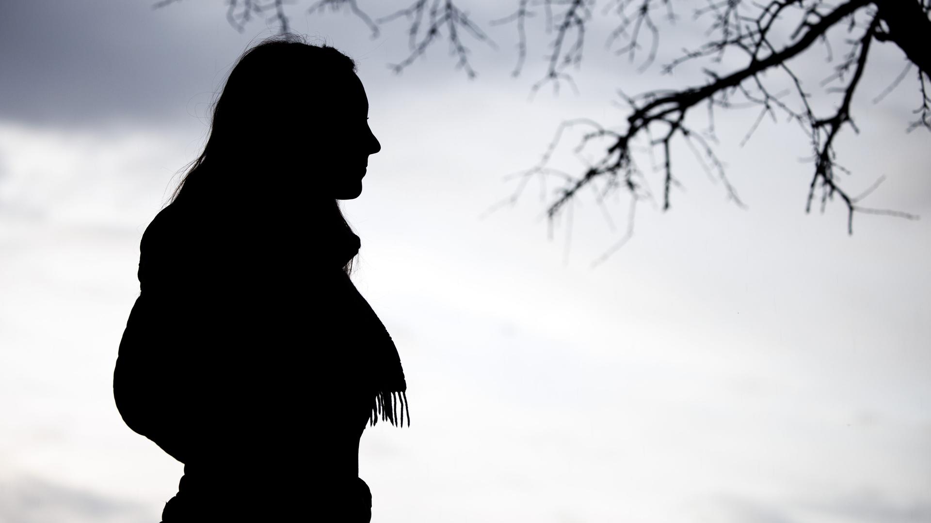 Eine Frau steht bei trübem Wetter unter einem kahlen Baum.