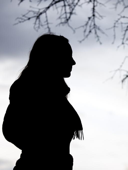 Eine Frau steht bei trübem Wetter unter einem kahlen Baum.