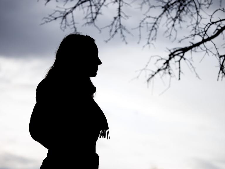 Eine Frau steht bei trübem Wetter unter einem kahlen Baum.