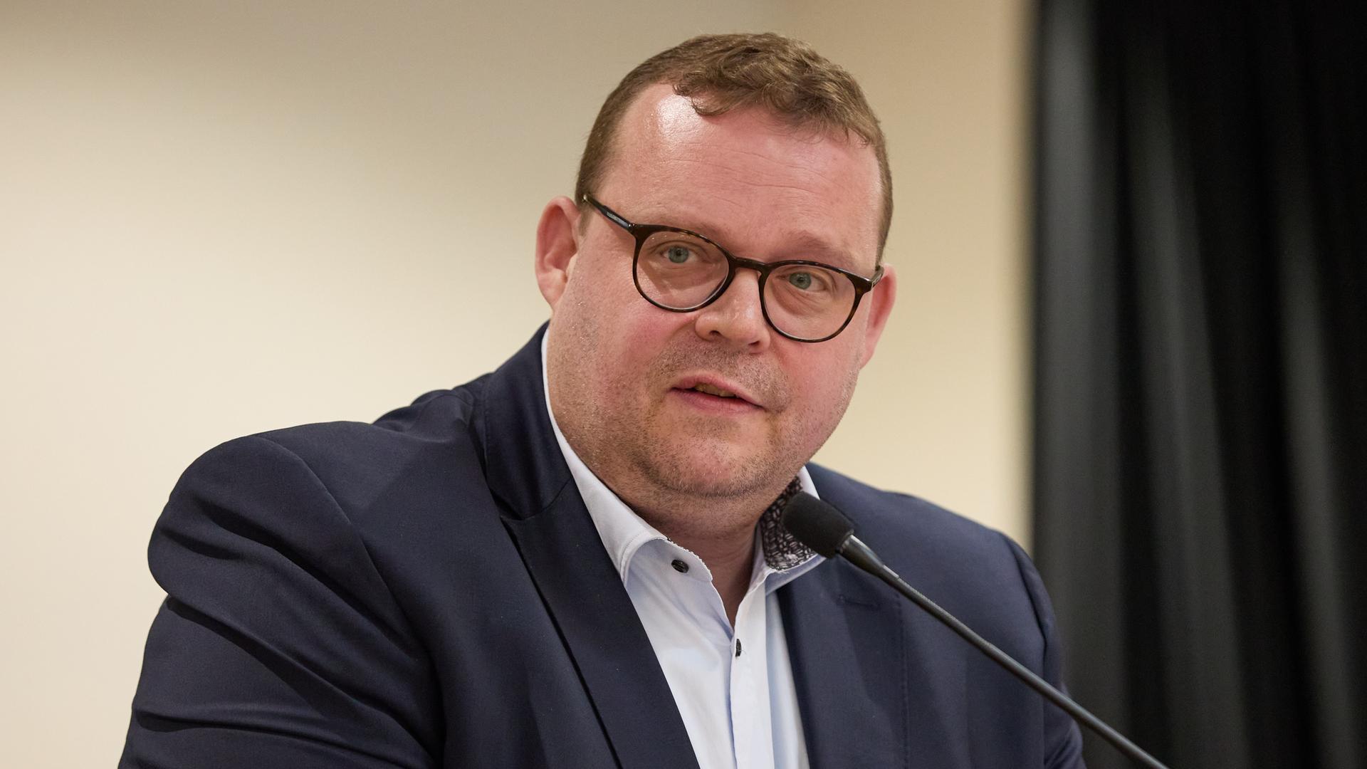 Zu sehen ist Ansgar Schledde, stellvertretender Landesvorsitzender der AfD Niedersachsen auf dem Landesparteitag am 20. April 2024. Ein korpulenter, mittelalter Mann im dunklen Jackett mit weißem Hemd sitzt an einem Mikrofon.