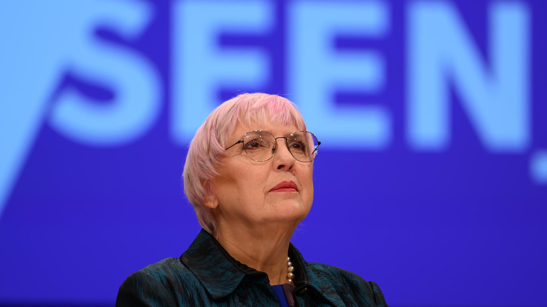 Claudia Roth steht vor einem blauen Hintergrund und blickt nach oben.