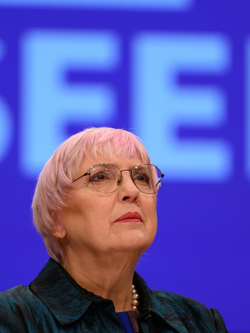 Claudia Roth steht vor einem blauen Hintergrund und blickt nach oben.