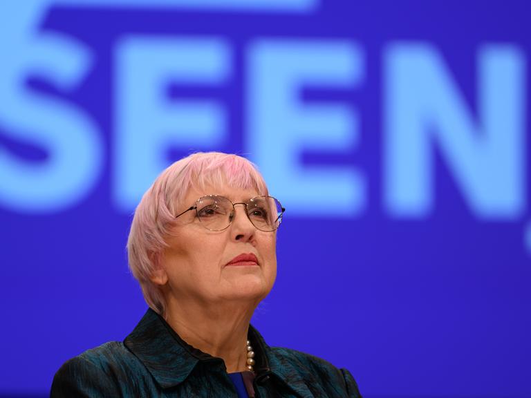 Claudia Roth steht vor einem blauen Hintergrund und blickt nach oben.