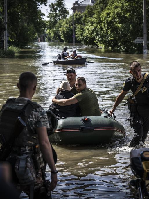Menschen werden aus überschwemmten Gebieten evakuiert, nachdem die Explosion im Wasserkraftwerk Kakhovka am 07. Juni 2023 in Cherson, Ukraine, zu Überschwemmungen geführt hat. Zu sehen ist eine überflutete Straße mit Zivilisten in Schlauchbooten und Soldaten, die Hilfe leisten.