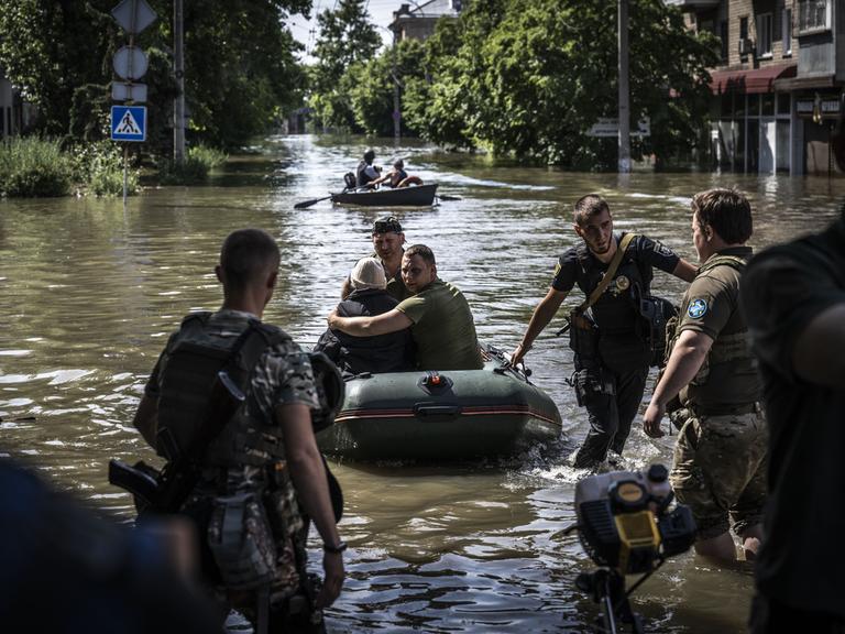 Menschen werden aus überschwemmten Gebieten evakuiert, nachdem die Explosion im Wasserkraftwerk Kakhovka am 07. Juni 2023 in Cherson, Ukraine, zu Überschwemmungen geführt hat. Zu sehen ist eine überflutete Straße mit Zivilisten in Schlauchbooten und Soldaten, die Hilfe leisten.