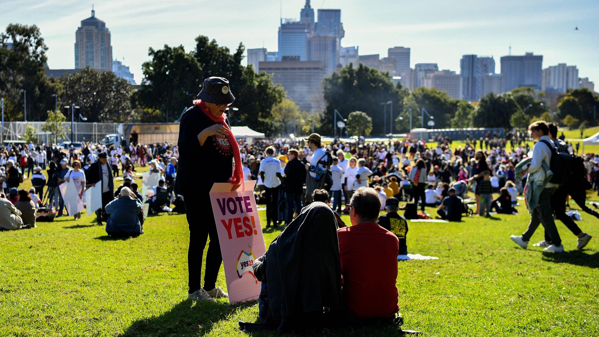 Menschen haben sich in Sydney in einem Park versammelt. Sie halten Schilder mit Aufschriften wie "Stimme mit Ja".