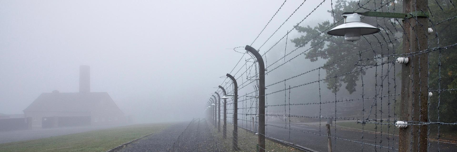 Rekonstruierter Lagerzaun mit Krematorium im Nebel in der Gedenkstätte des ehemaligen KZ Buchenwald.