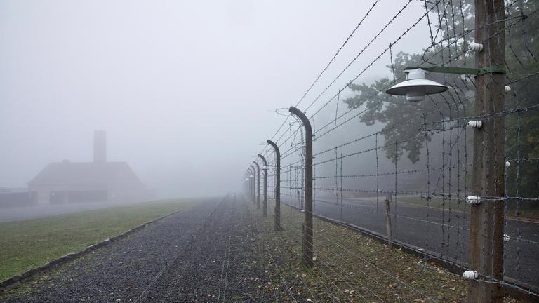 Rekonstruierter Lagerzaun mit Krematorium im Nebel in der Gedenkstätte des ehemaligen KZ Buchenwald.