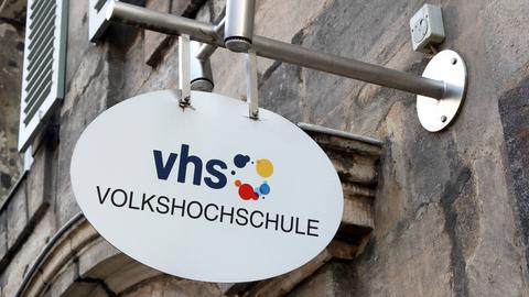 Ein Schild mit der Aufschrift vhs Volkshochschule hängt an einer Hauswand