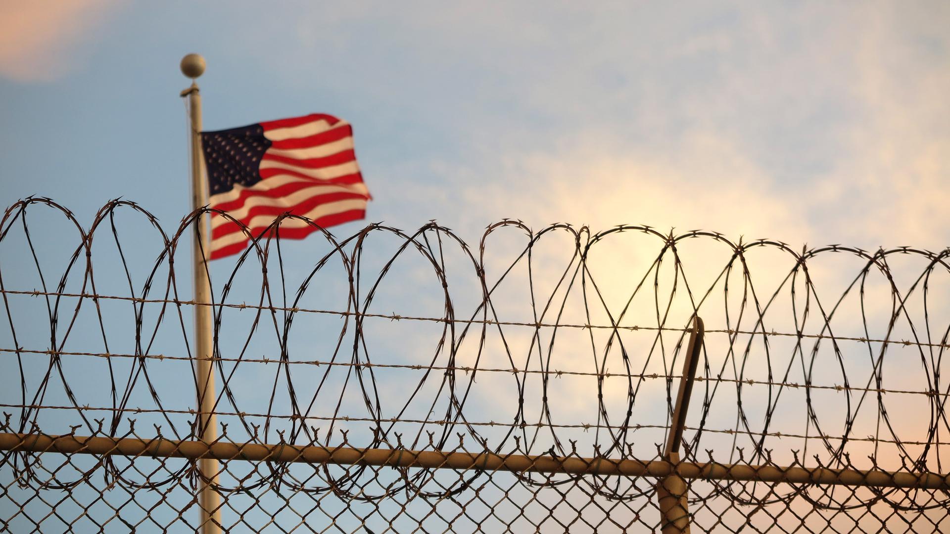 Eine US-Flagge weht hinter einem Stacheldrahtzaun in Guantanamo