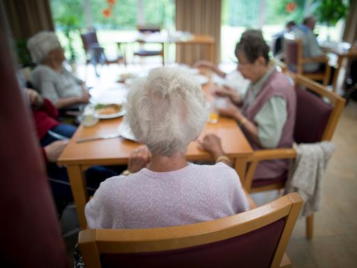 Bewohner in einem Altenpflegeheim sitzen beim Mittagessen an einem Tisch im Essensraum. 