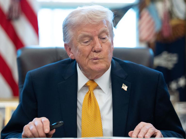 US-Präsident Trump sitzt am Schreibtisch im Oval Office und zieht eine Grimasse.