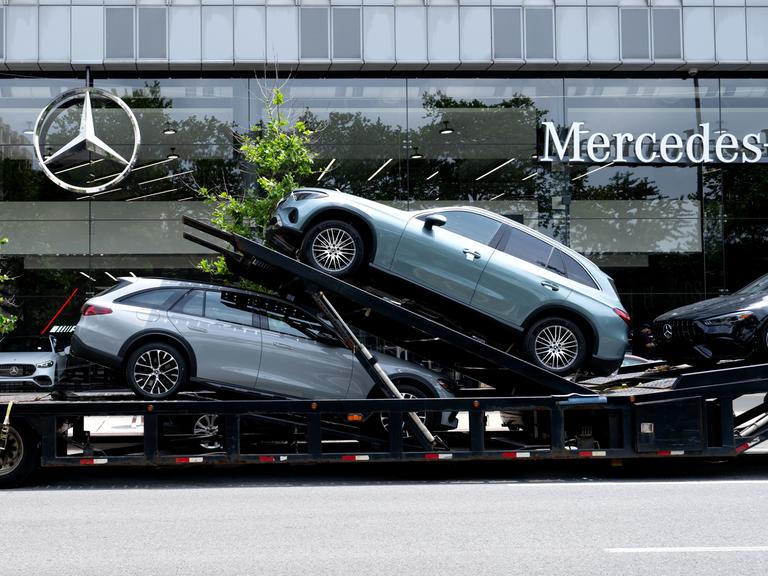 Ein Autotransporter mit Neuwagen von Mercedes-Benz steht vor einem Autohaus in Manhattan.