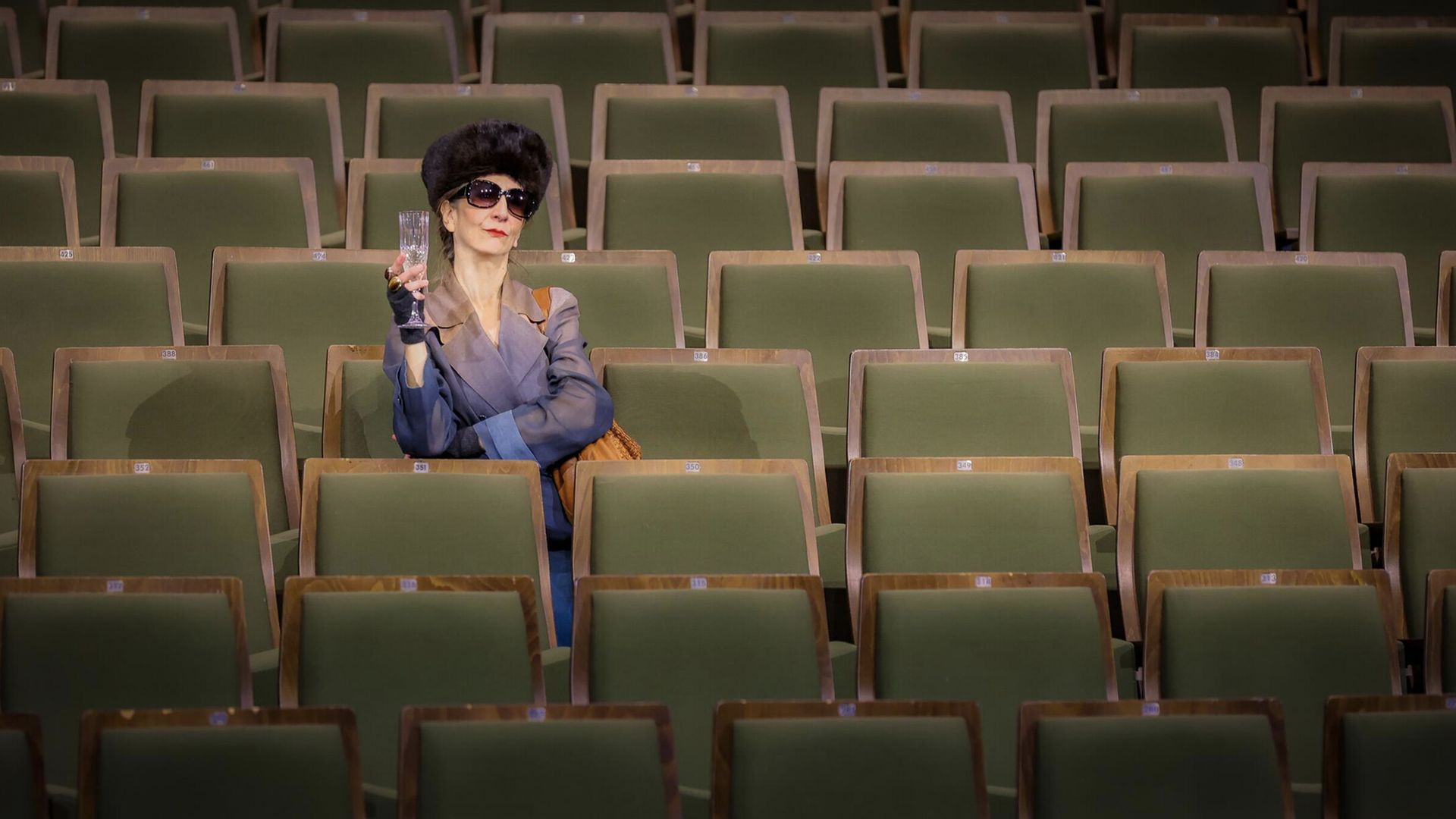 Claudia Hübbecke als Irmgard Keun sitzt mit einem Glas Sekt in der Hand im Zuschauerraum.