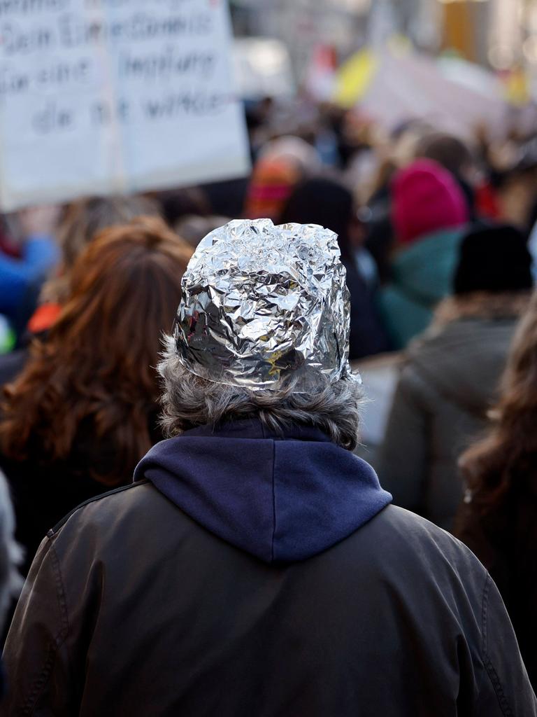 Eine Person mit einem Aluhut auf einer Demonstration gegen die Impflicht.