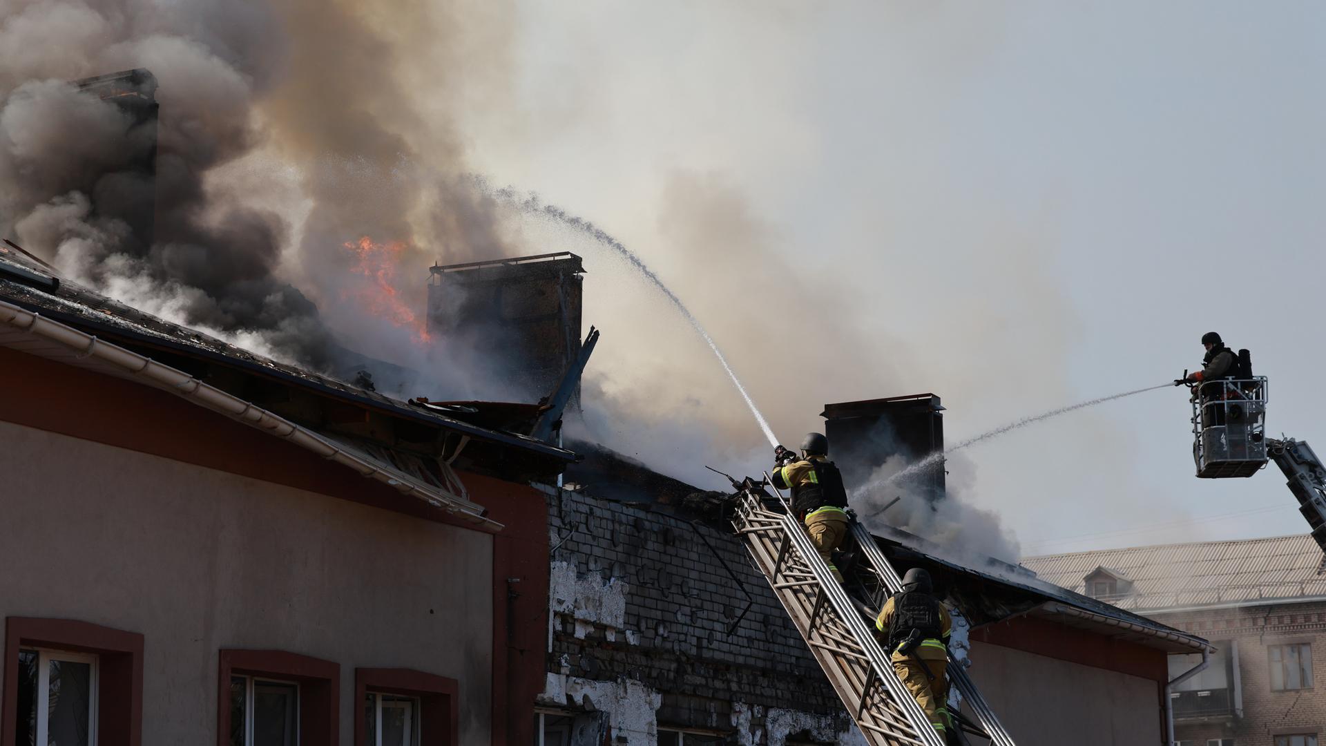Rettungskräfte versuchen, ein Feuer in einem Gebäude zu löschen, das nach einem russischen Drohnenangriff auf Saporischschja in der Ukraine brennt.