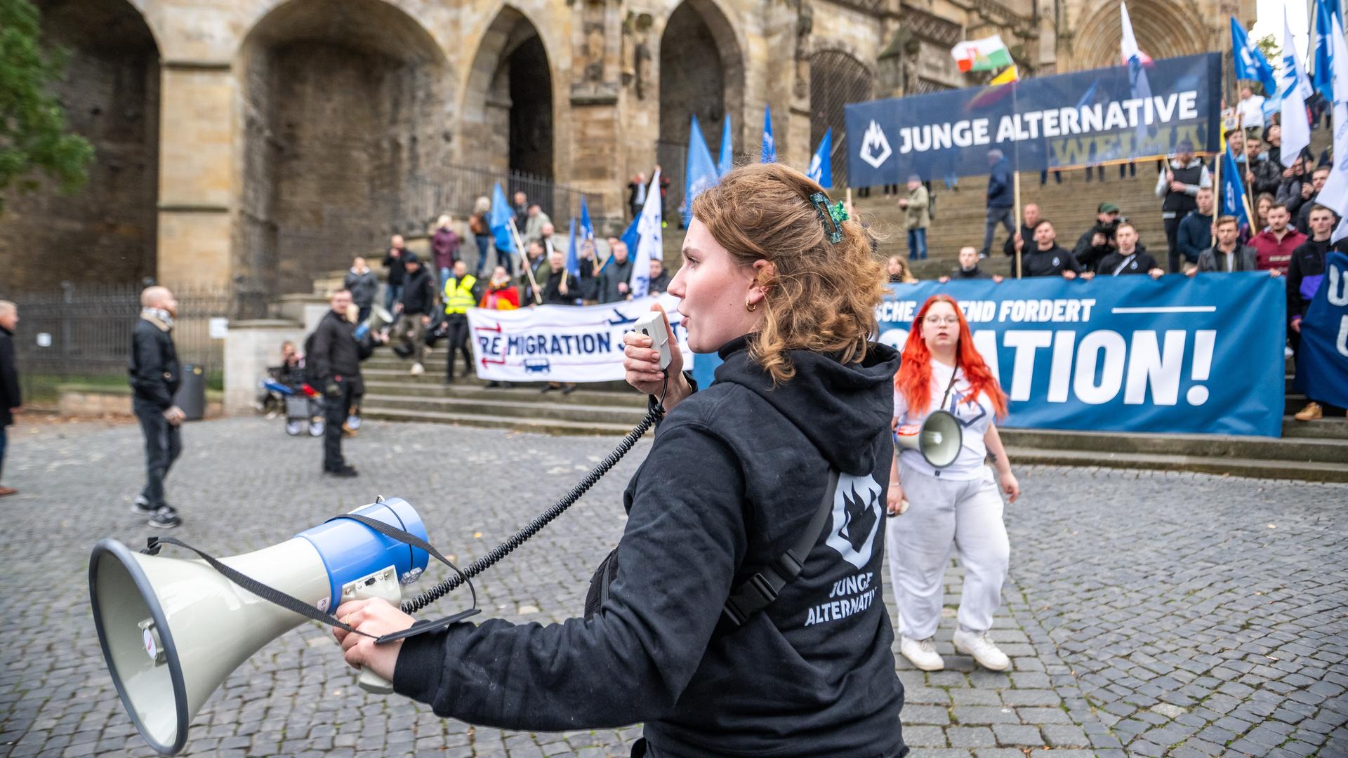 Die "Junge Alternative" posiert auf den Domstufen für ein Gruppenfoto während der Demonstration der AfD unter dem Motto: "Der Osten steht zusammen", eine junge Frau ruft in ein Megafon, Erfurt 2023.