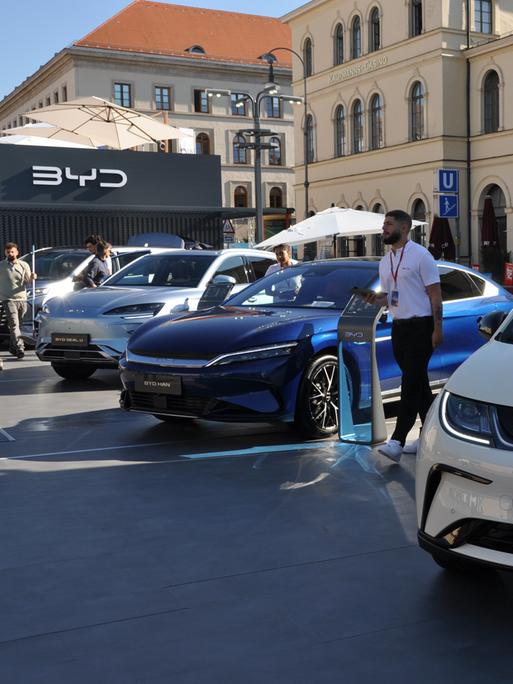 Mehrere Elektroautos stehen vor einer Halle auf der Münchener Automesse IAA.