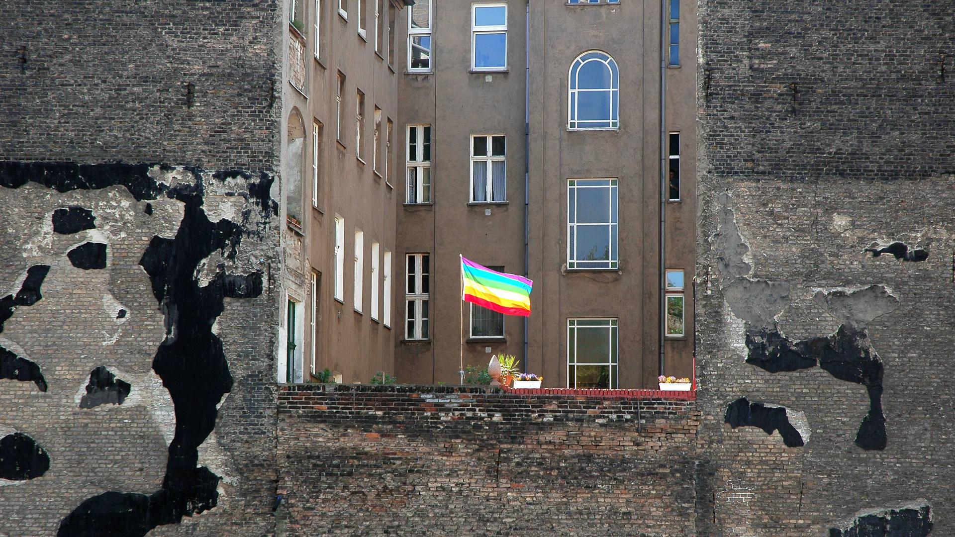Eine Regenbogenfahne als Zeichen der Schwulen- und Lesbenbewegung weht  in einem Hinterhof zwischen typischen Berliner Altbauhäusern.