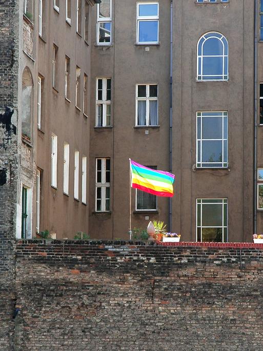 Eine Regenbogenfahne als Zeichen der Schwulen- und Lesbenbewegung weht  in einem Hinterhof zwischen typischen Berliner Altbauhäusern.
