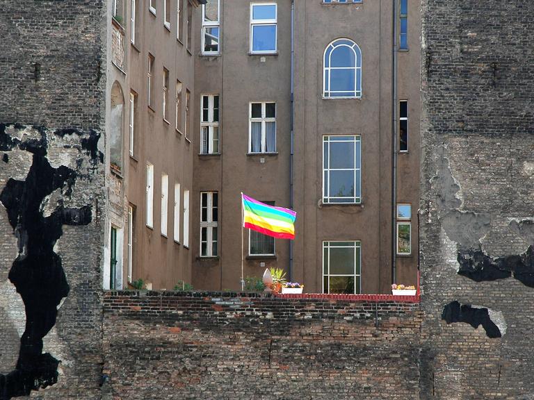 Eine Regenbogenfahne als Zeichen der Schwulen- und Lesbenbewegung weht  in einem Hinterhof zwischen typischen Berliner Altbauhäusern.