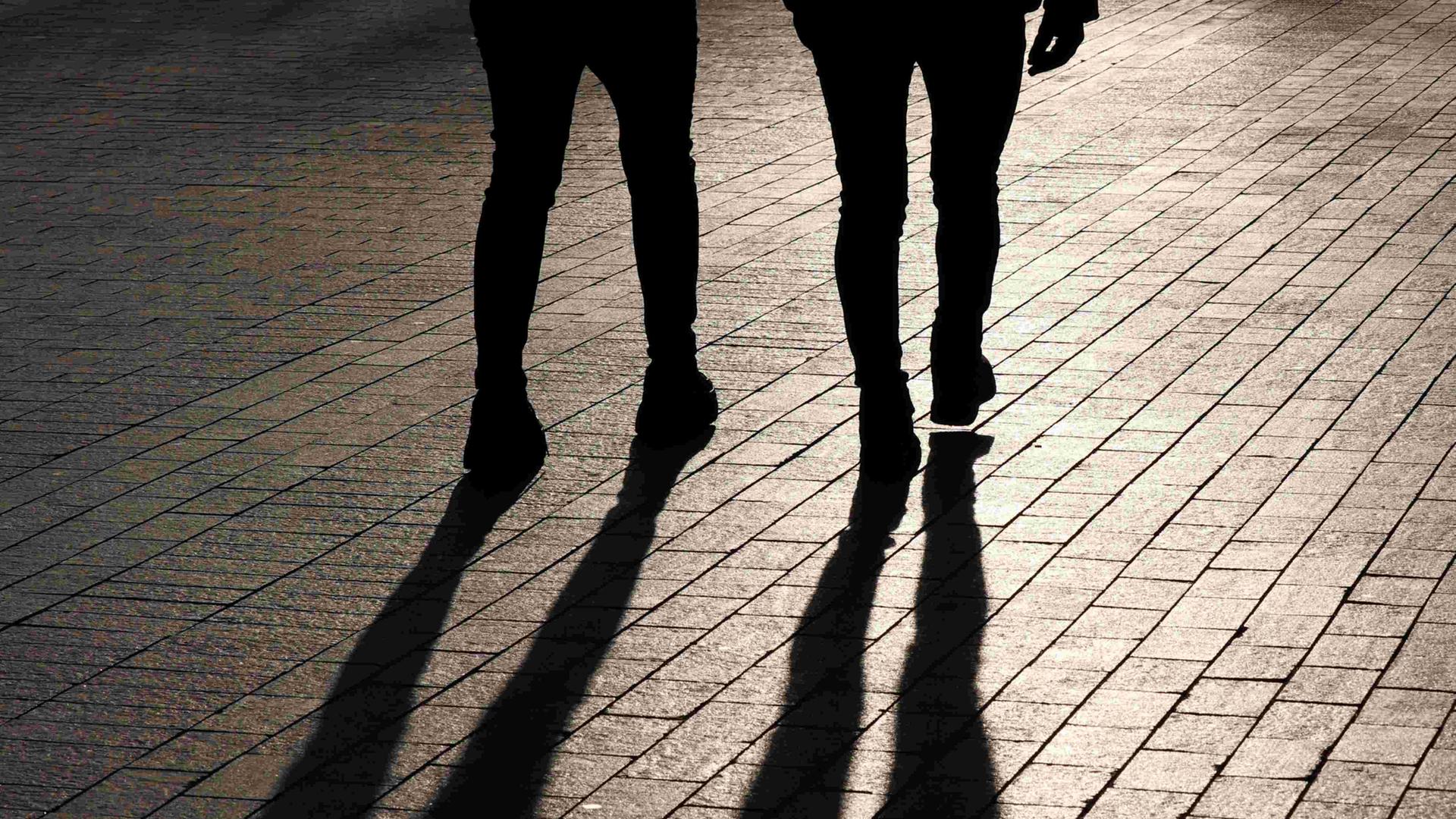 Die Beine zweier nebeneinander gehender Menschen von hinten - samt Schattenwurf.