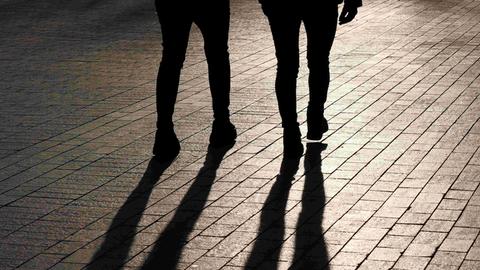 Die Beine zweier nebeneinander gehender Menschen von hinten - samt Schattenwurf.