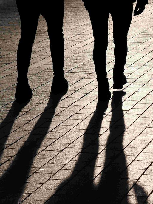 Die Beine zweier nebeneinander gehender Menschen von hinten - samt Schattenwurf.