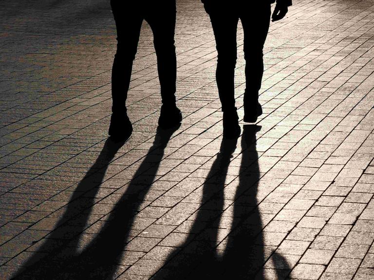 Die Beine zweier nebeneinander gehender Menschen von hinten - samt Schattenwurf.