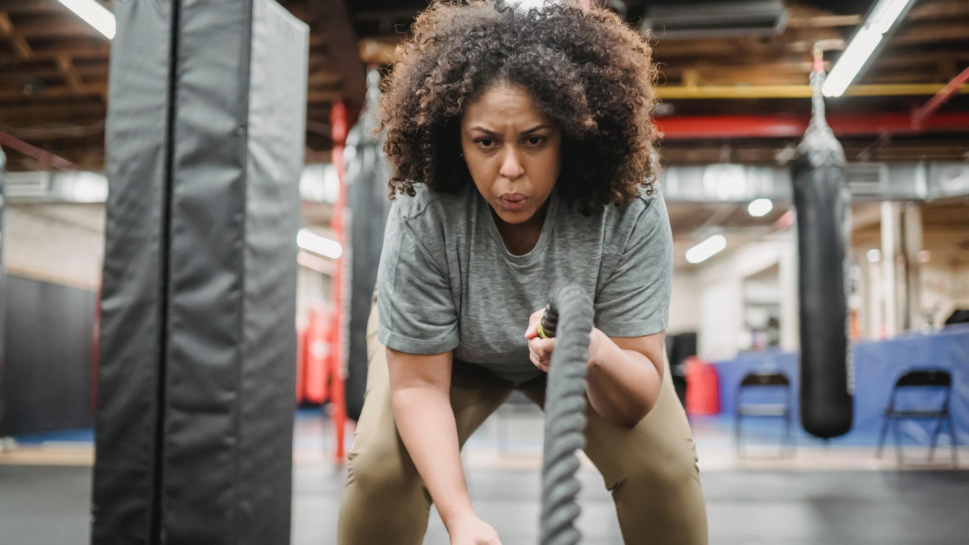 Entschlossene Frau beim Training mit Kampfseilen im Fitnessstudio Entschlossene Frau beim Training mit Kampfseilen im Fitnessstudio