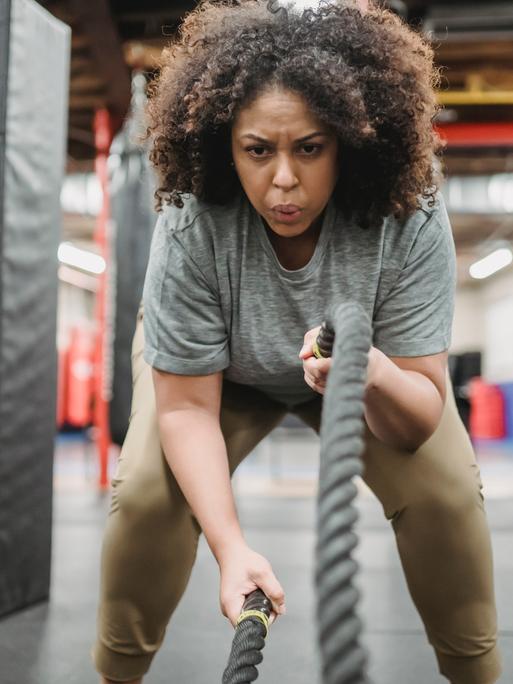 Entschlossene Frau beim Training mit Kampfseilen im Fitnessstudio Entschlossene Frau beim Training mit Kampfseilen im Fitnessstudio