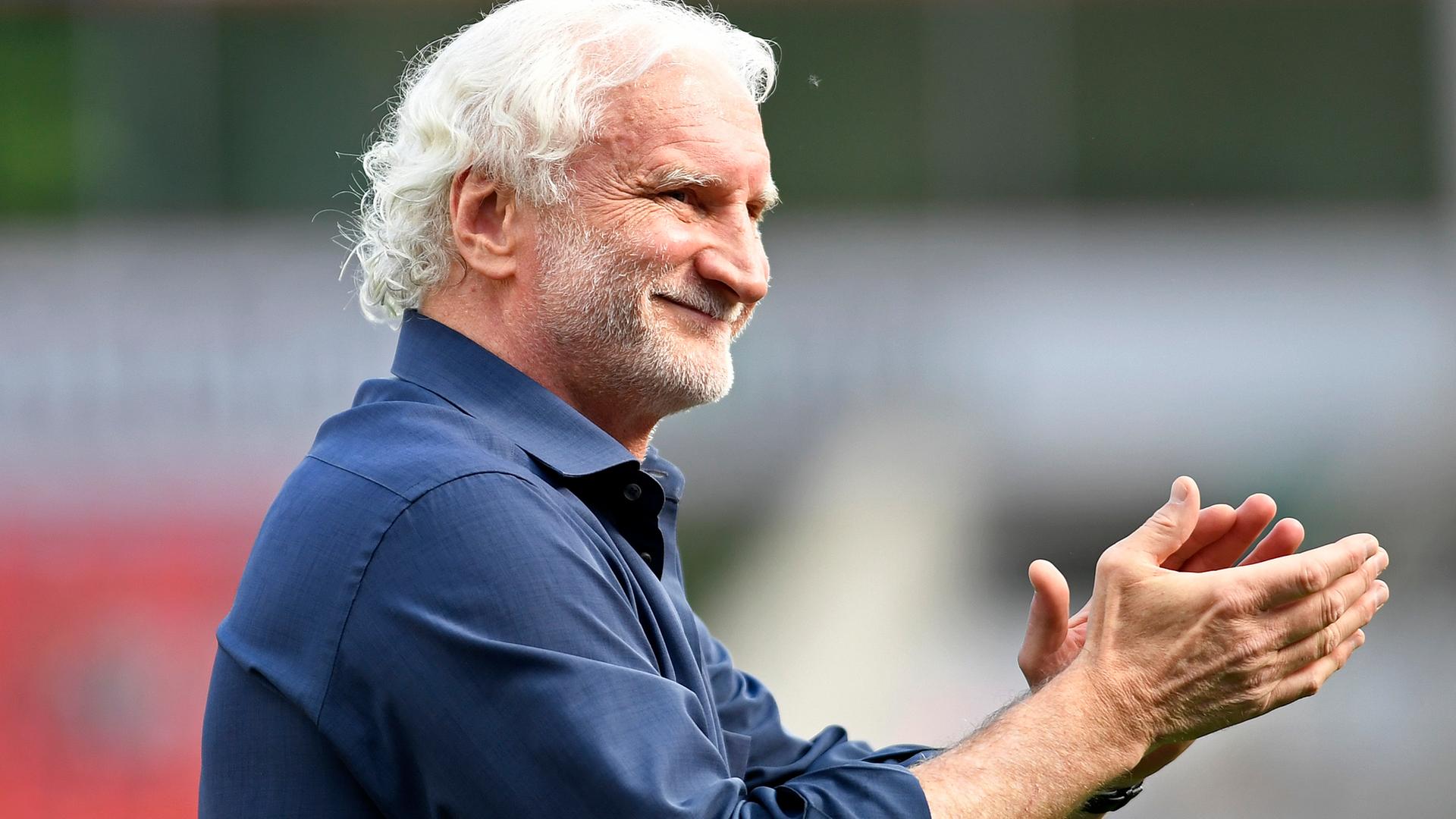Das Bild zeigt den ehemaligen Fußballer und Nationaltrainer Rudi Völler. Er trägt ein blaues Hemd, lächelt breit und klatscht in die Hände.