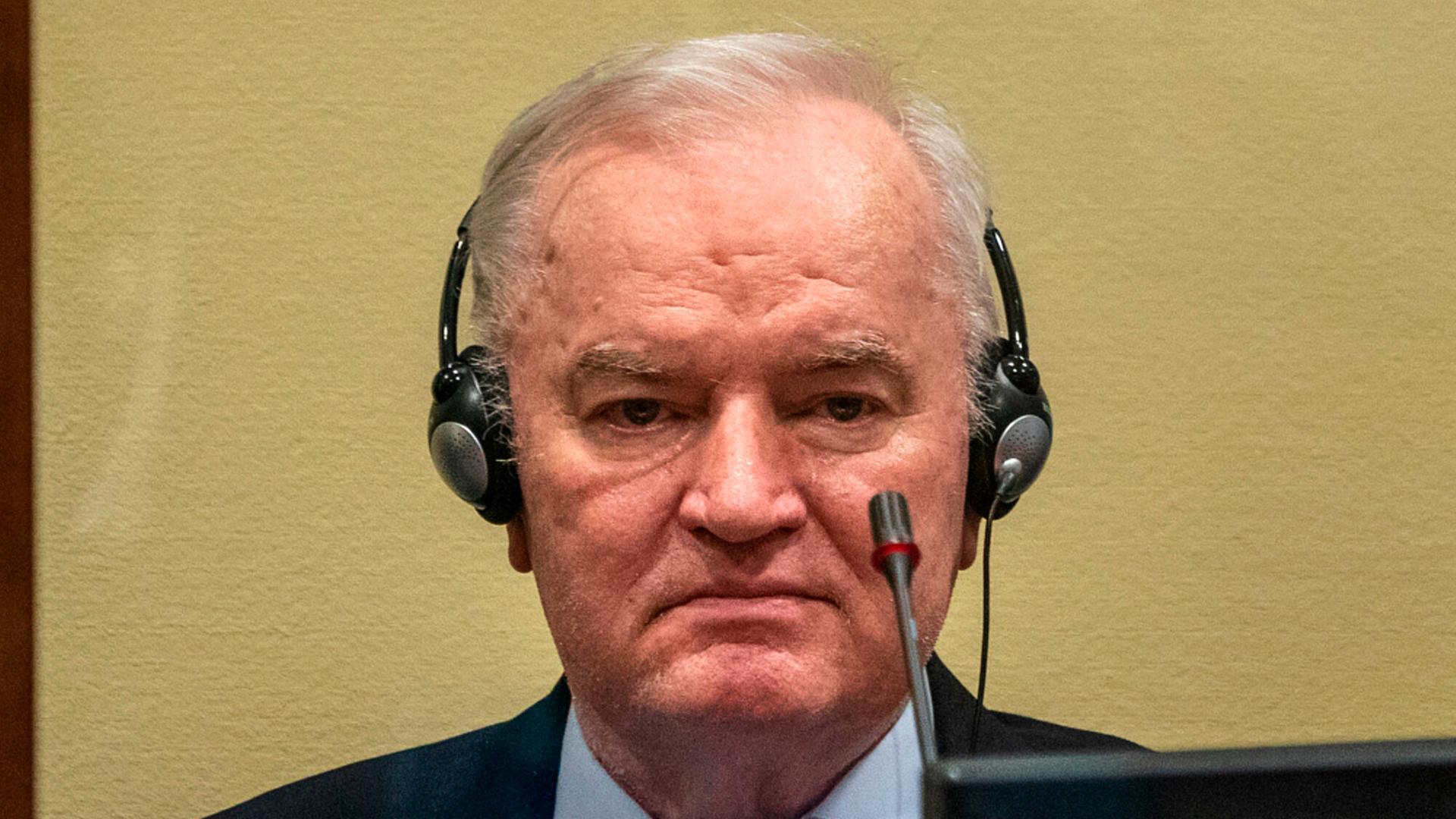 Ratko Mladic mit ernstem Blick vor einer beigen Wand im Porträt, er hat Kopfhörer auf.
