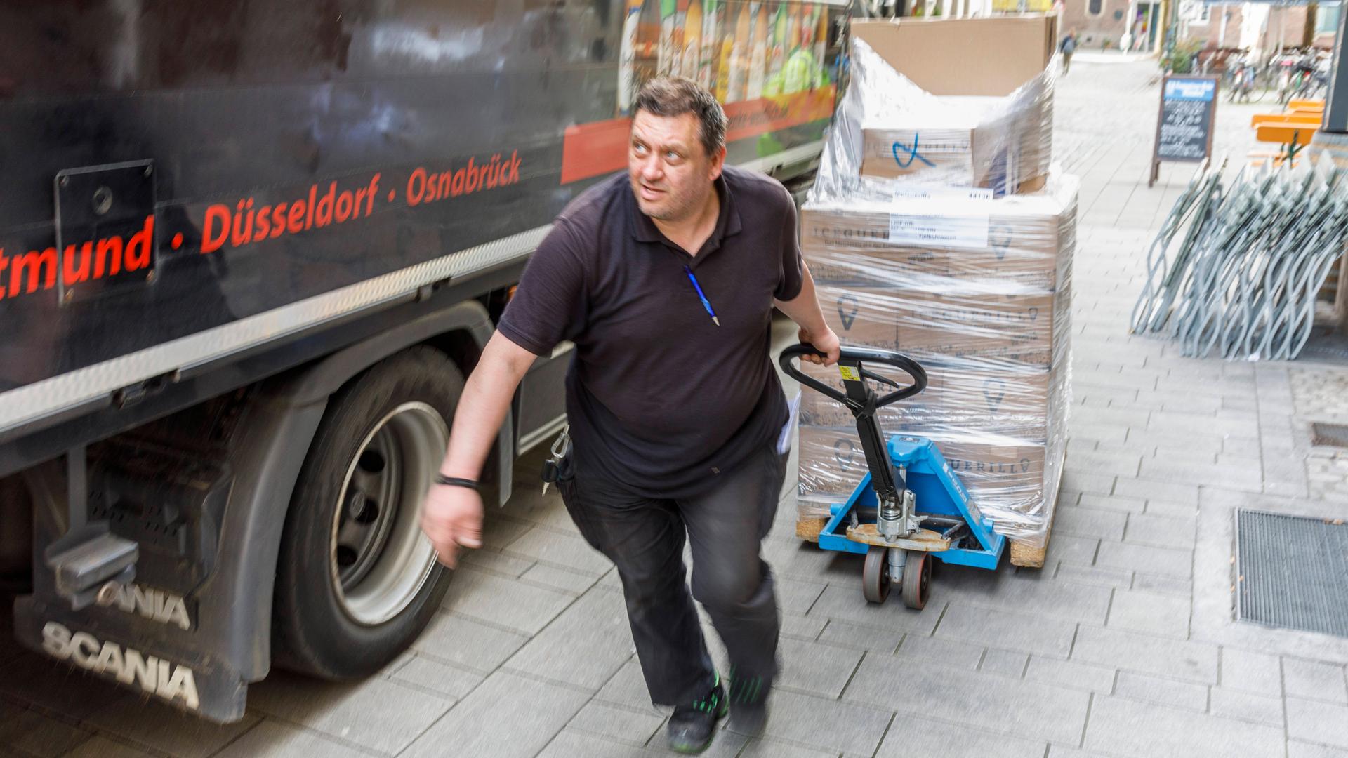 Ein Mann zieht einen beladenen Hubwagen an einem LKW vorbei
