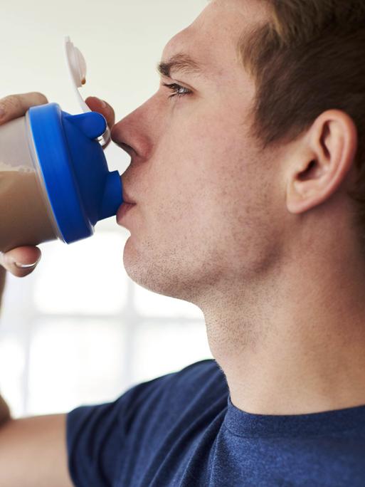 Ein junger Mann trinkt einen Protein-Shake aus seiner Sportflasche.