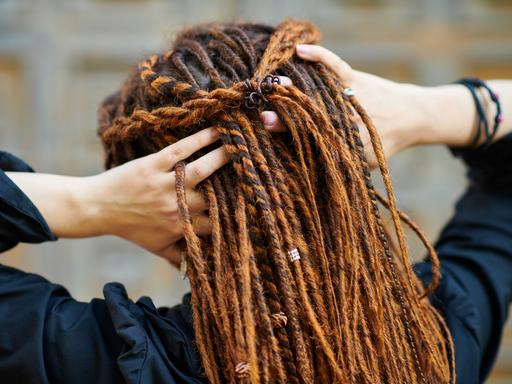 Eine weiße Frau fasst sich am Hinterkopf in ihre Dreadlocks. 
