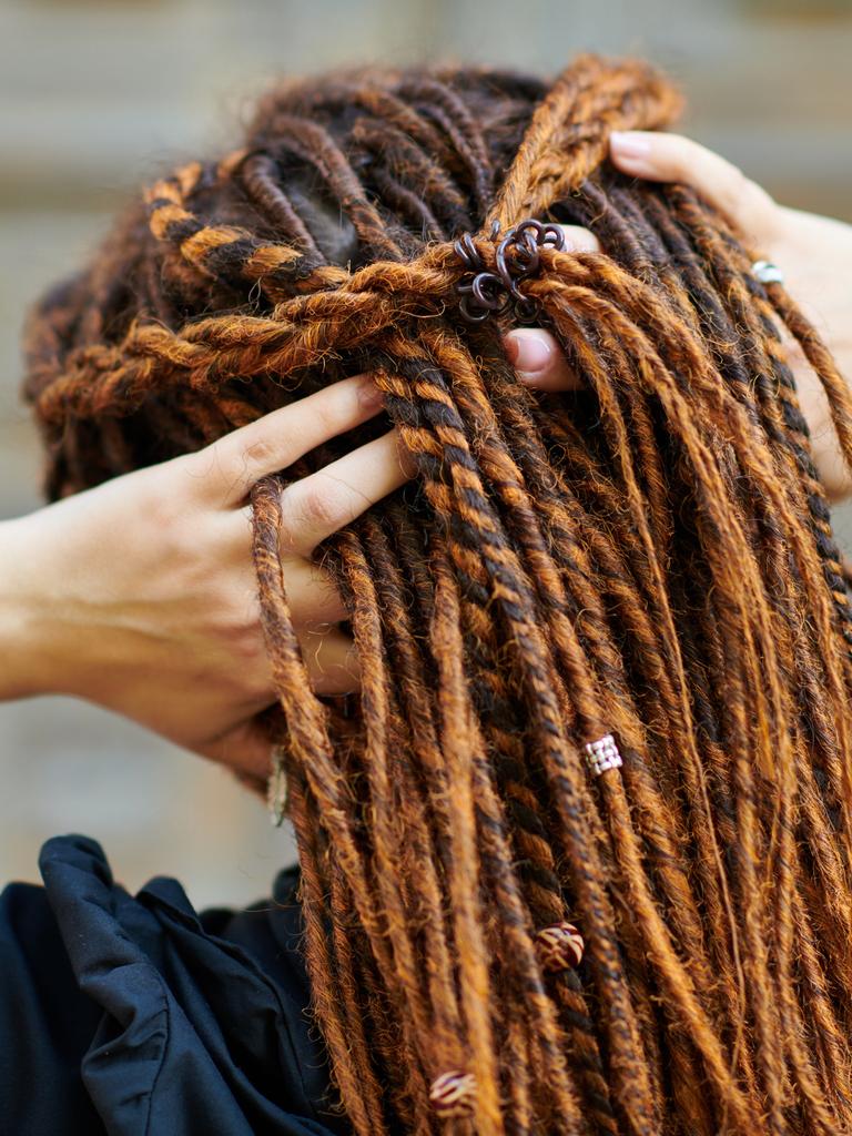 Eine weiße Frau fasst sich am Hinterkopf in ihre Dreadlocks. 