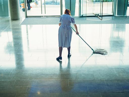 Eine Frau in Arbeitskleidung wischt den Boden einer Hotellobby.
