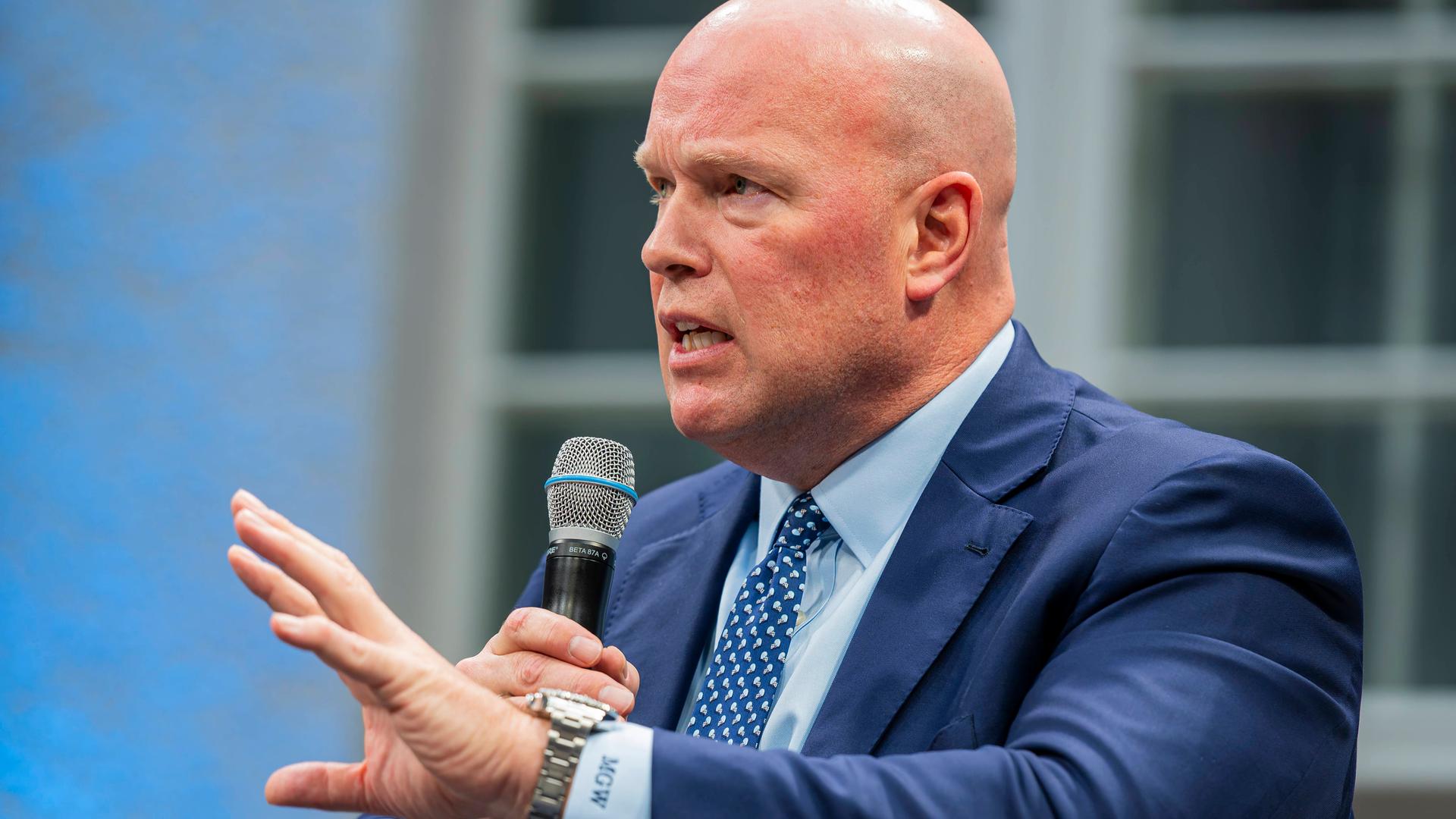 Matthew Whitaker, US-Botschafter bei der NATO, hat ein Mikrofon in rechten Hand und gestikuliert mit der linken, um seine Worte zu unterstreichen.